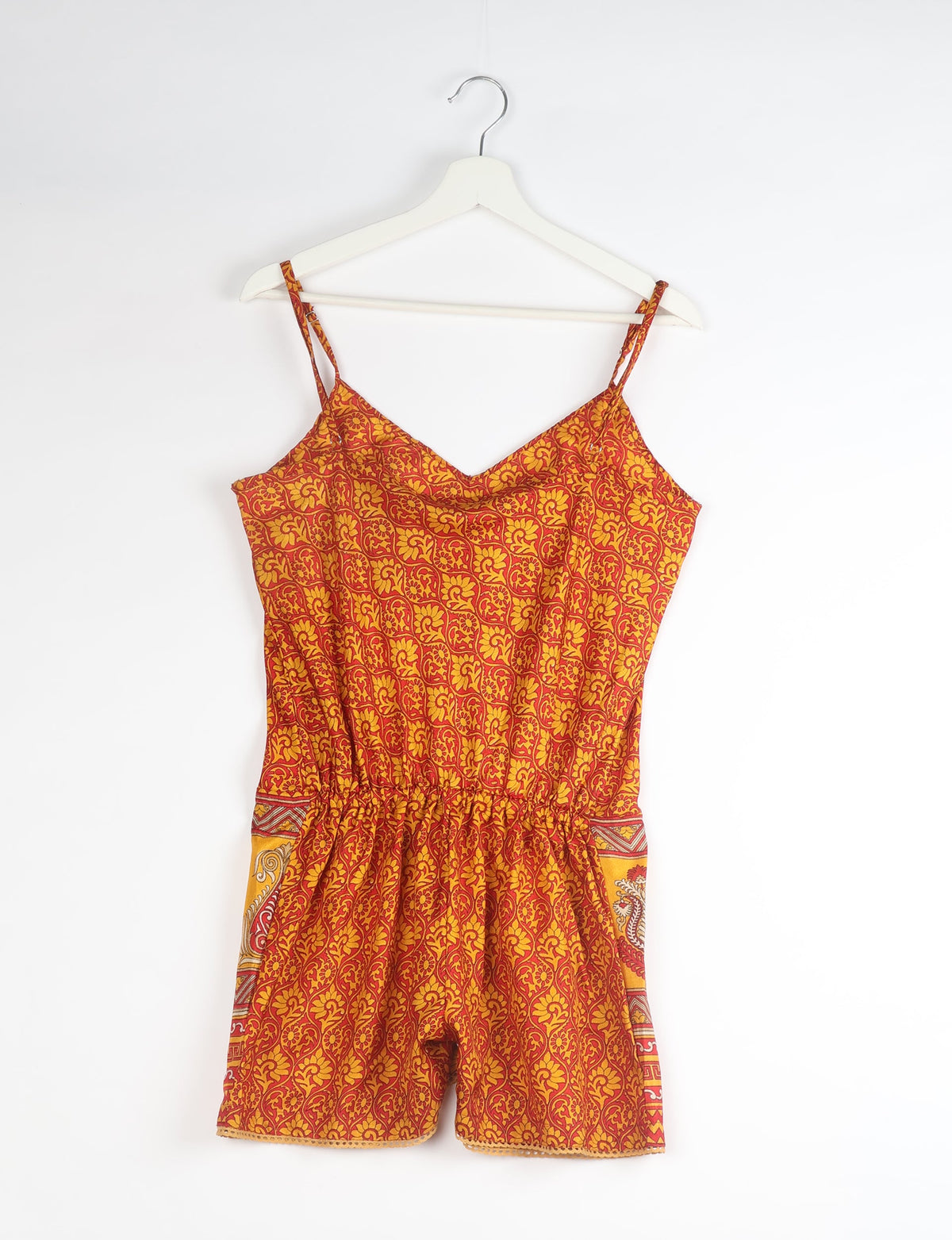 Orange and red abstract patterned playsuit with thin straps and elastic waist, hanging on white hanger, front view