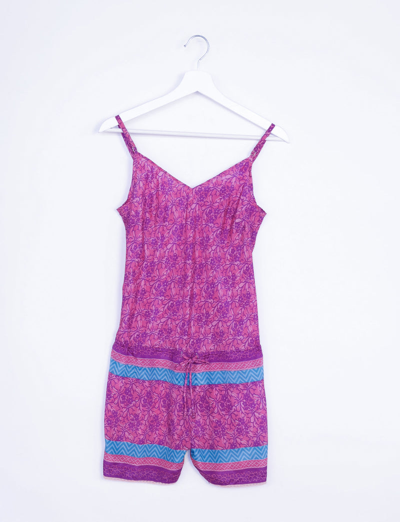 Pink tropical playsuit with lace trim, adjustable straps, and blue and purple patterned bands, hanging on a white hanger