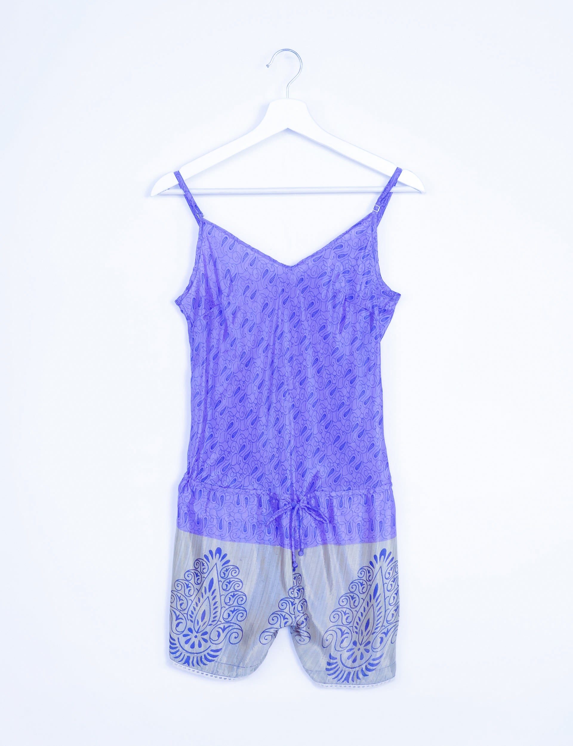 Purple playsuit with adjustable straps, micro paisley lace design on top, and blue patterned shorts, hanging on white hanger