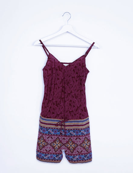 Red playsuit with abstract swirl pattern on top and multicolor geometric border print on shorts, hanging on white hanger