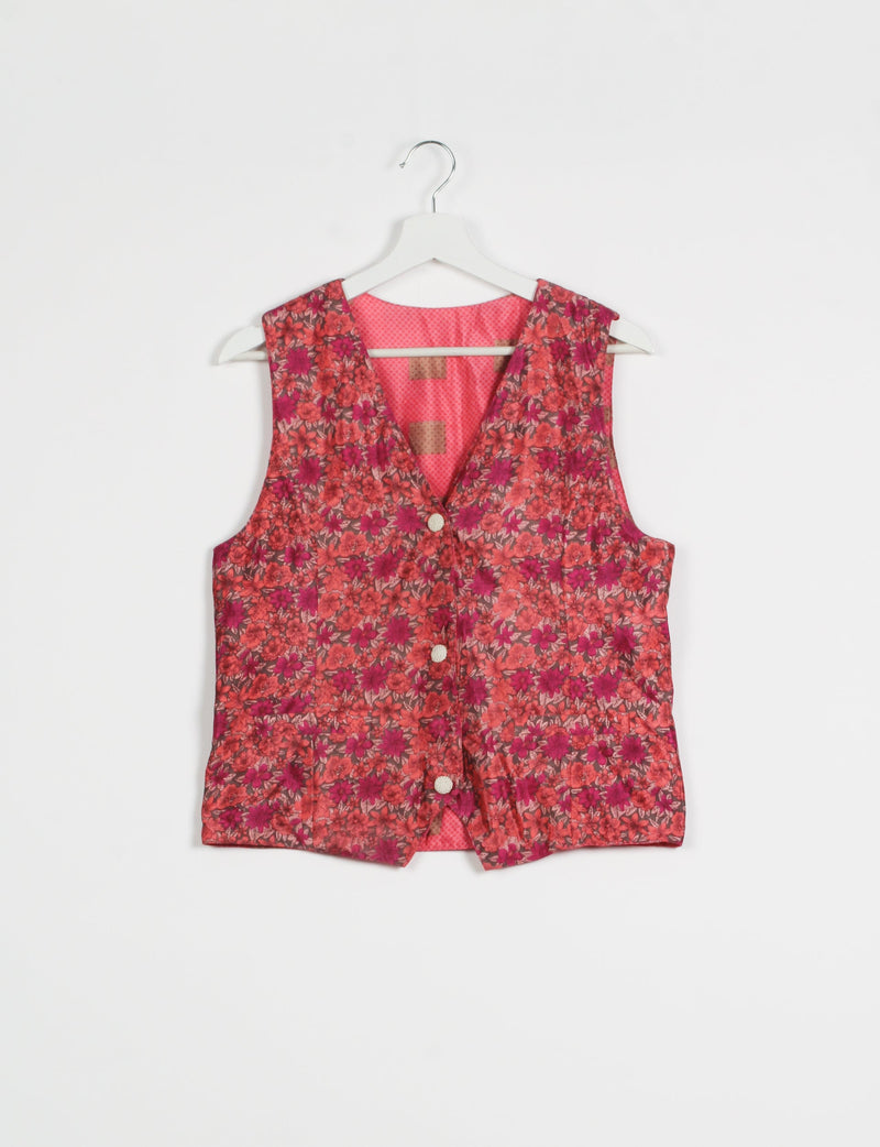Pink floral sleeveless waistcoat with front buttons, V-neckline, and contrasting pink patterned lining, hanging on white hanger