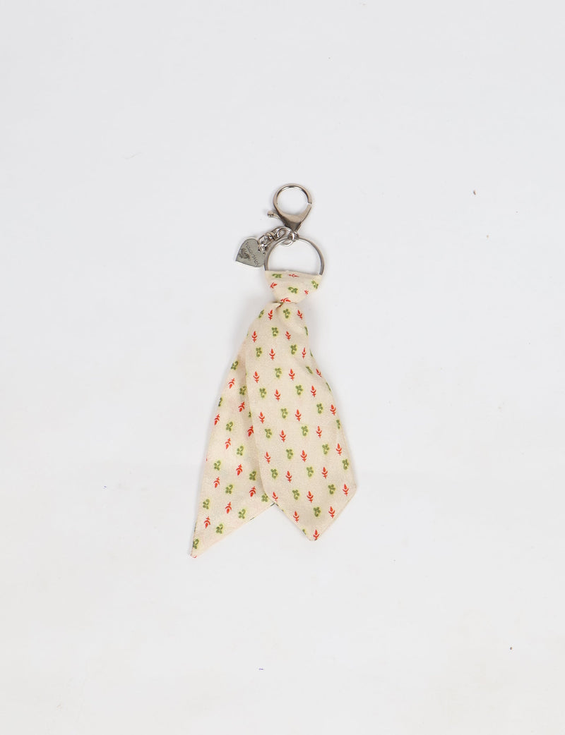 Beige fabric tie keychain with small red and green floral micro design and silver metal clasp with heart charm