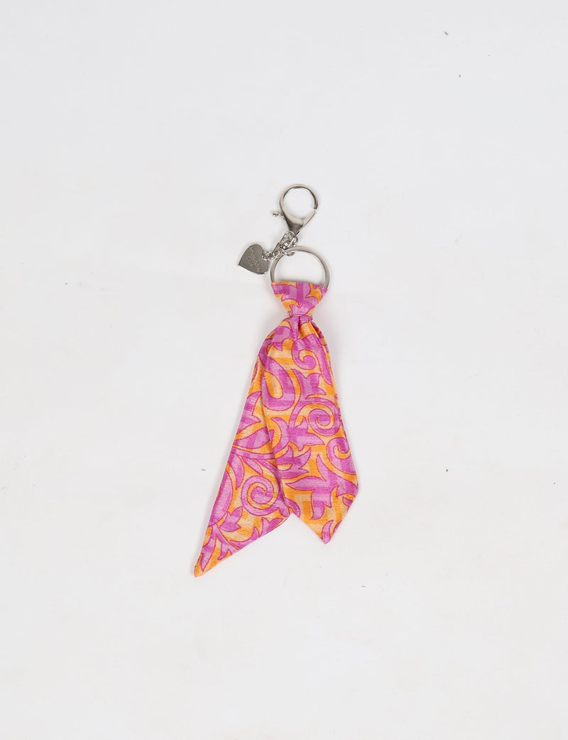 Pink and orange tropical patterned fabric tie keychain with silver ring and heart-shaped charm, flat lay on white background
