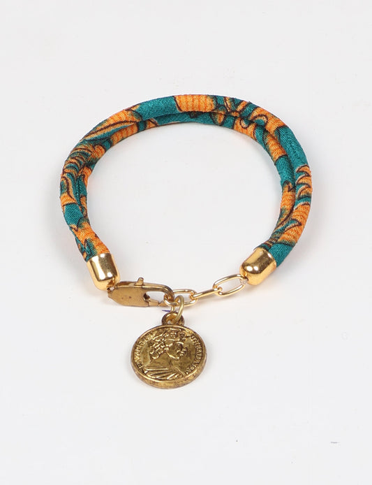 A close-up image of a hand wearing the Sari Rope Bracelete with Charm, showcasing its colorful threads and unique design. This accessory embodies ethical fashion and sustainability, crafted from repurposed saris for a stylish and eco-conscious statement.