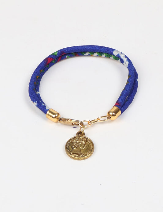 A close-up image of a hand wearing the Sari Rope Bracelete with Charm, showcasing its colorful threads and unique design. This accessory embodies ethical fashion and sustainability, crafted from repurposed saris for a stylish and eco-conscious statement.