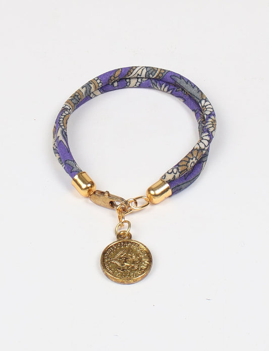 A close-up image of a hand wearing the Sari Rope Bracelete with Charm, showcasing its colorful threads and unique design. This accessory embodies ethical fashion and sustainability, crafted from repurposed saris for a stylish and eco-conscious statement.