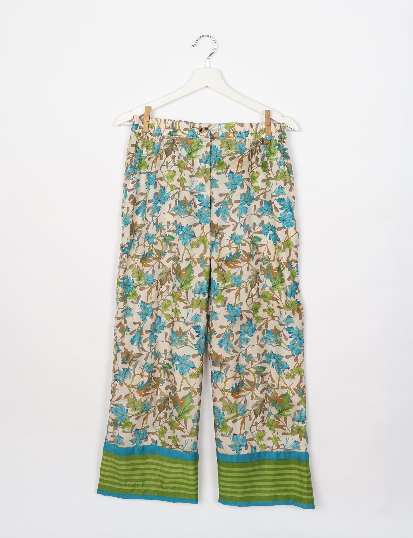 Beige lounge pants with blue and green leaf print, elastic waistband, button closure, and green striped hem with blue trim