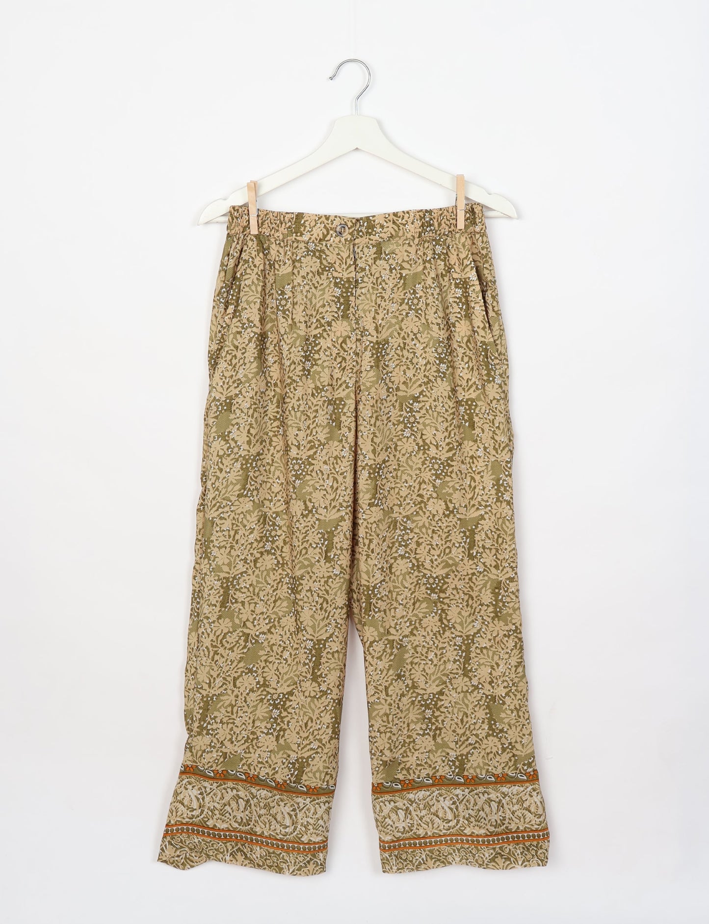 Beige tropical print lounge pants with button closure, elastic waistband, side pockets, and patterned hem, hanging on white