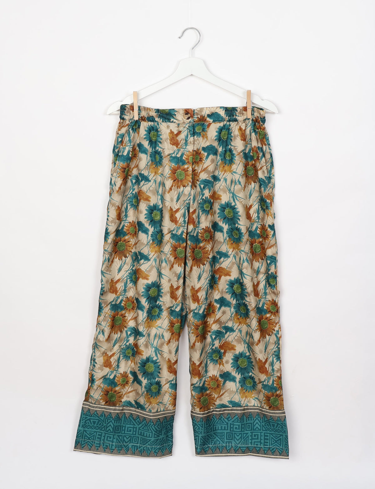 Beige floral lounge pants with teal and brown flower print and teal geometric border, hanging on white hanger front view