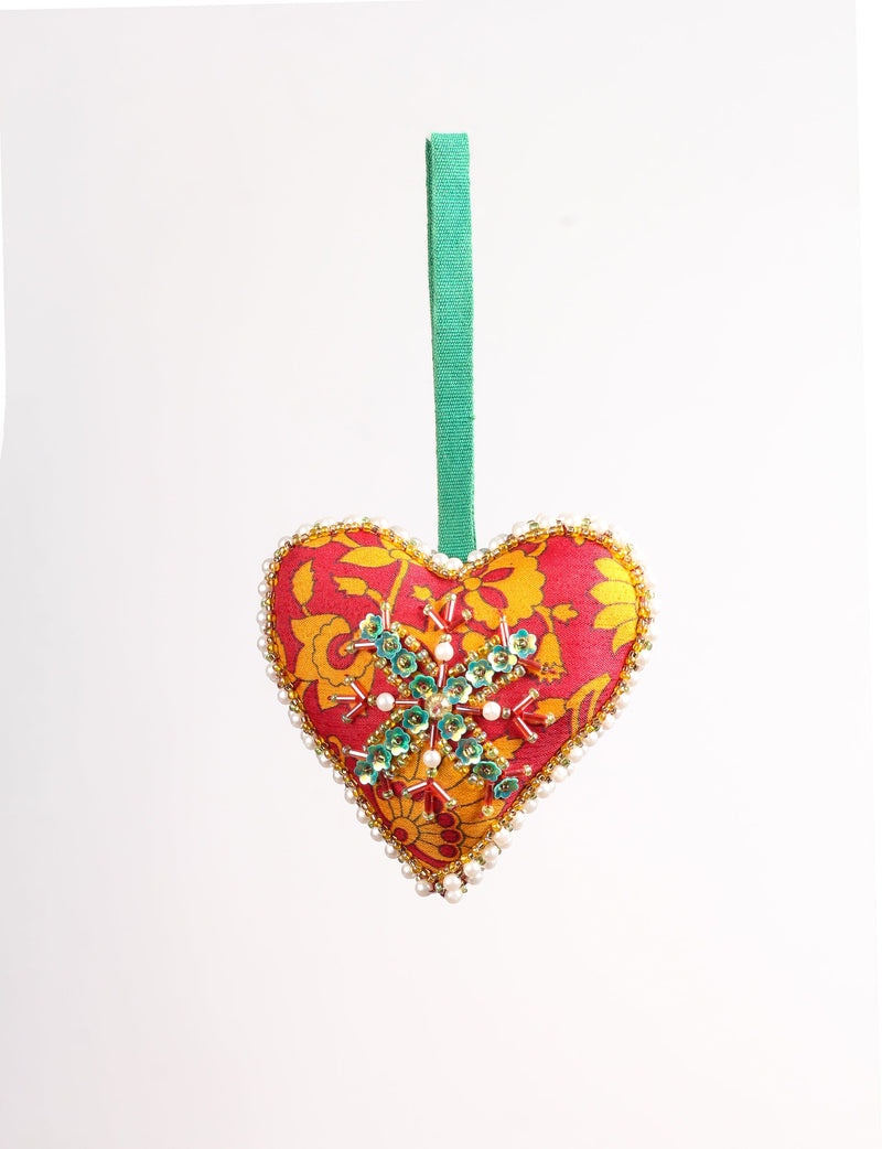 Red heart-shaped fabric ornament with yellow floral pattern, green beaded snowflake, pearl and gold bead trim, and green