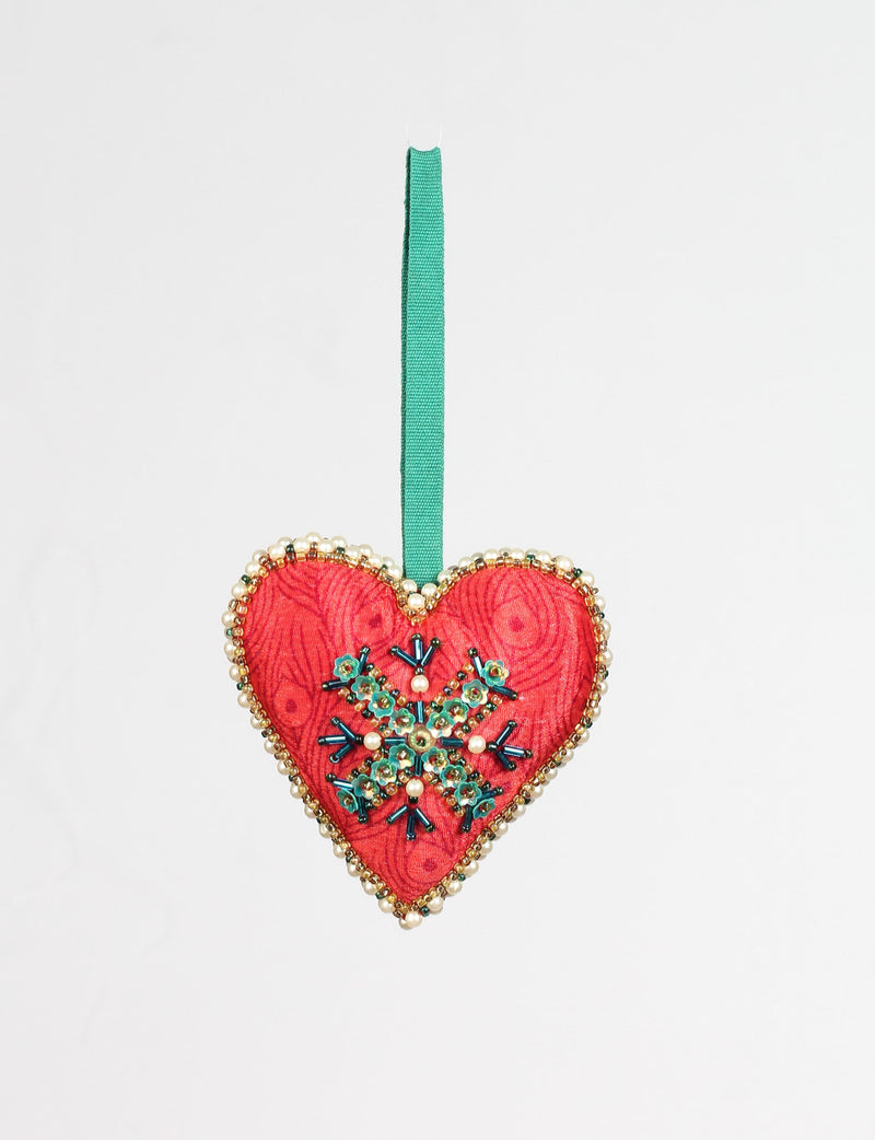 Red heart-shaped ornament with abstract pattern, green and pearl bead snowflake design, and green hanging ribbon