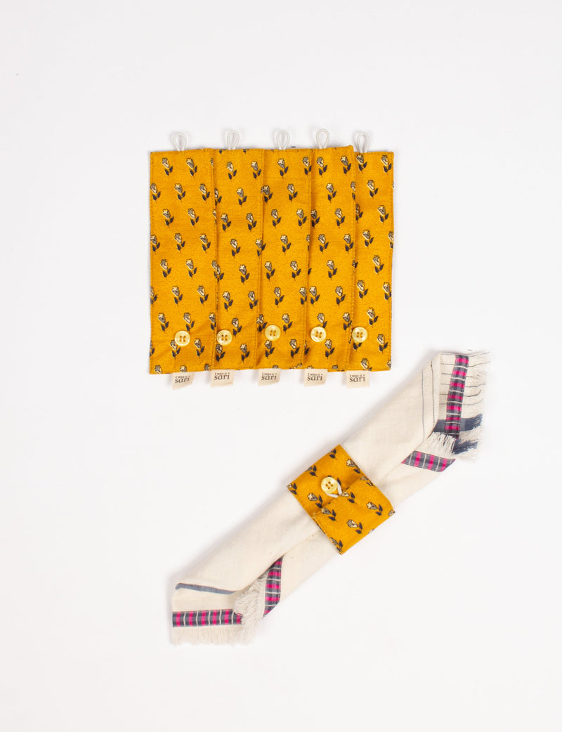 Set of six mustard yellow fabric napkin rings with small floral print and buttons, shown flat and on a folded napkin