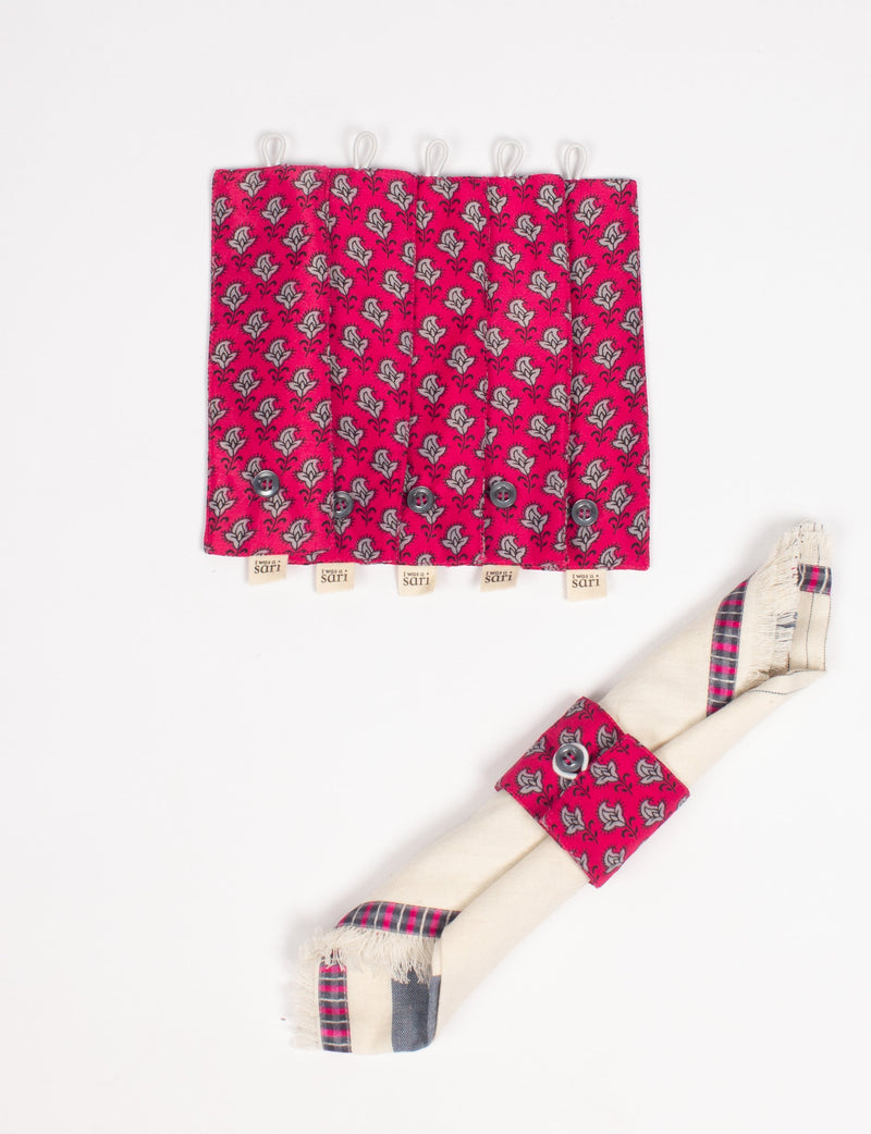 Set of six pink fabric napkin rings with gray floral pattern, black buttons, and "I was a sari" tags, shown flat and on a napkin