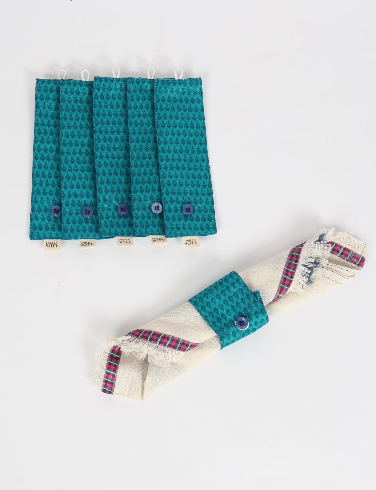 Set of six blue fabric napkin rings with micro teardrop pattern and button closure, one holding a rolled napkin with plaid trim