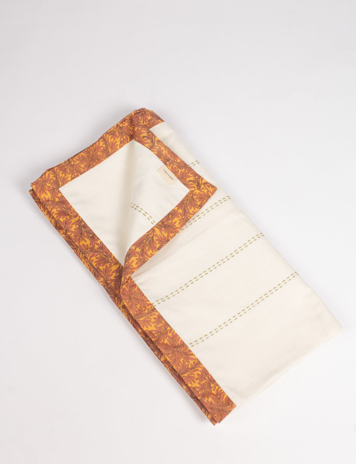 Folded cotton sofa throw in off-white with broad yellow and brown floral sari edging and stitched line details