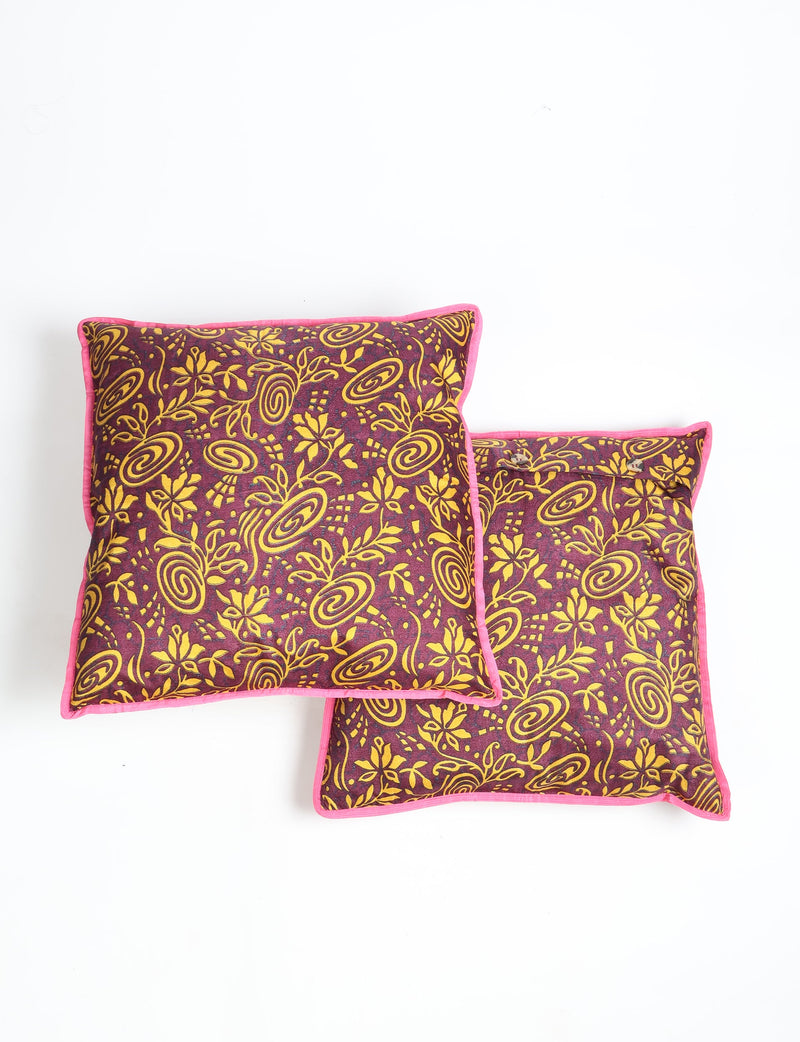 Set of two red cushion covers with yellow tropical floral and swirl patterns, pink piping edges, shown flat on white background