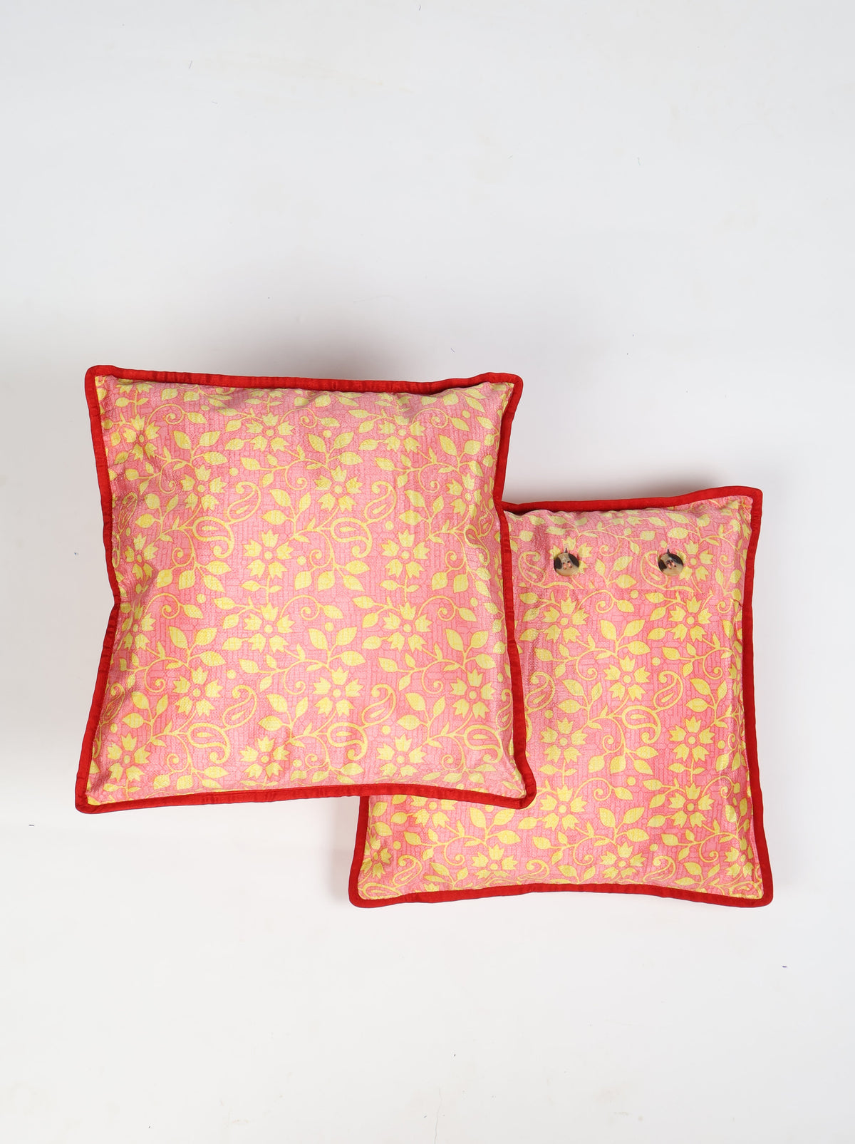 Set of two pink cushion covers with yellow floral pattern and red piping edges, one showing button closure, flat lay view