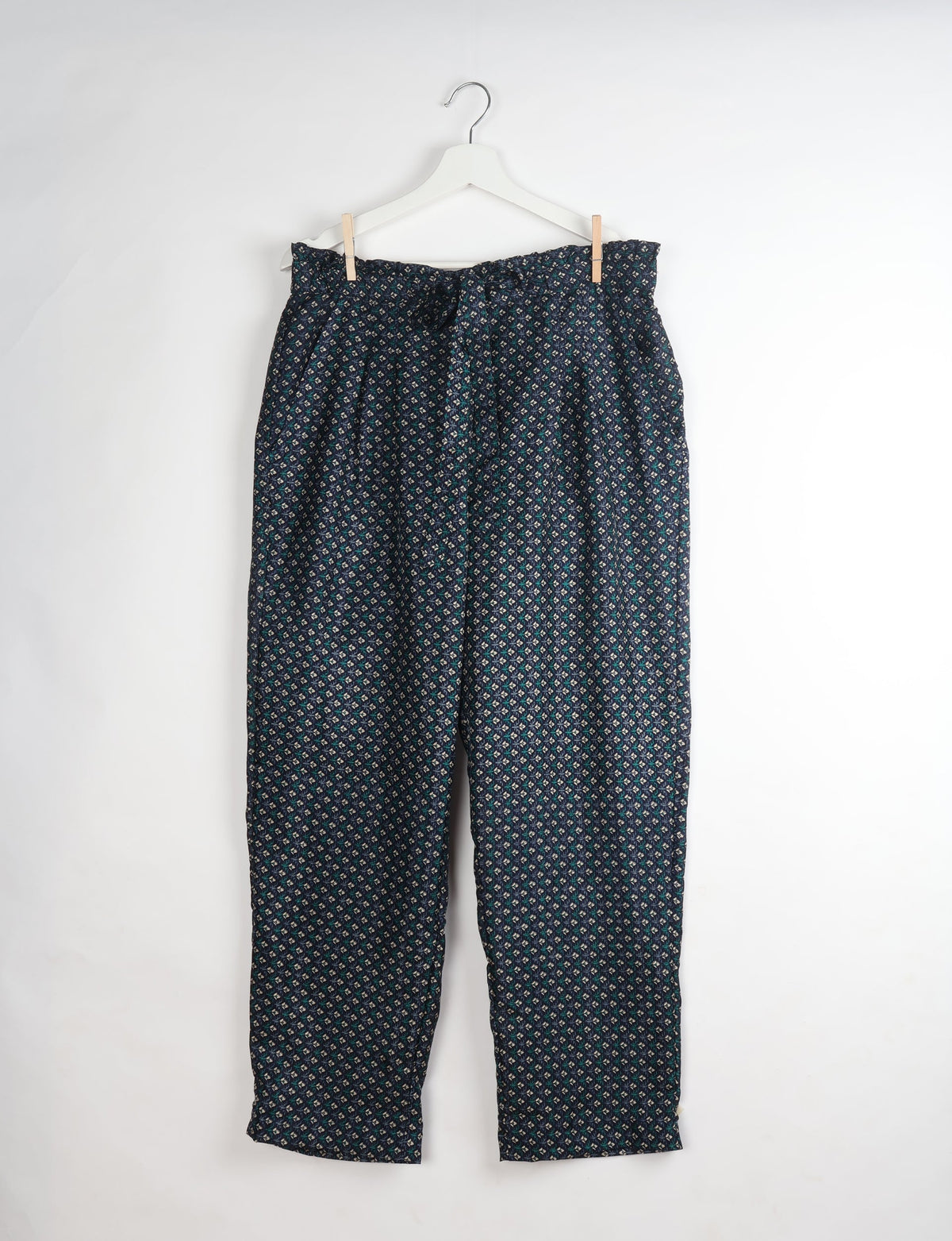 Blue paperbag high-waisted pull-on pants with a small geometric pattern, hanging on a white hanger against a white background