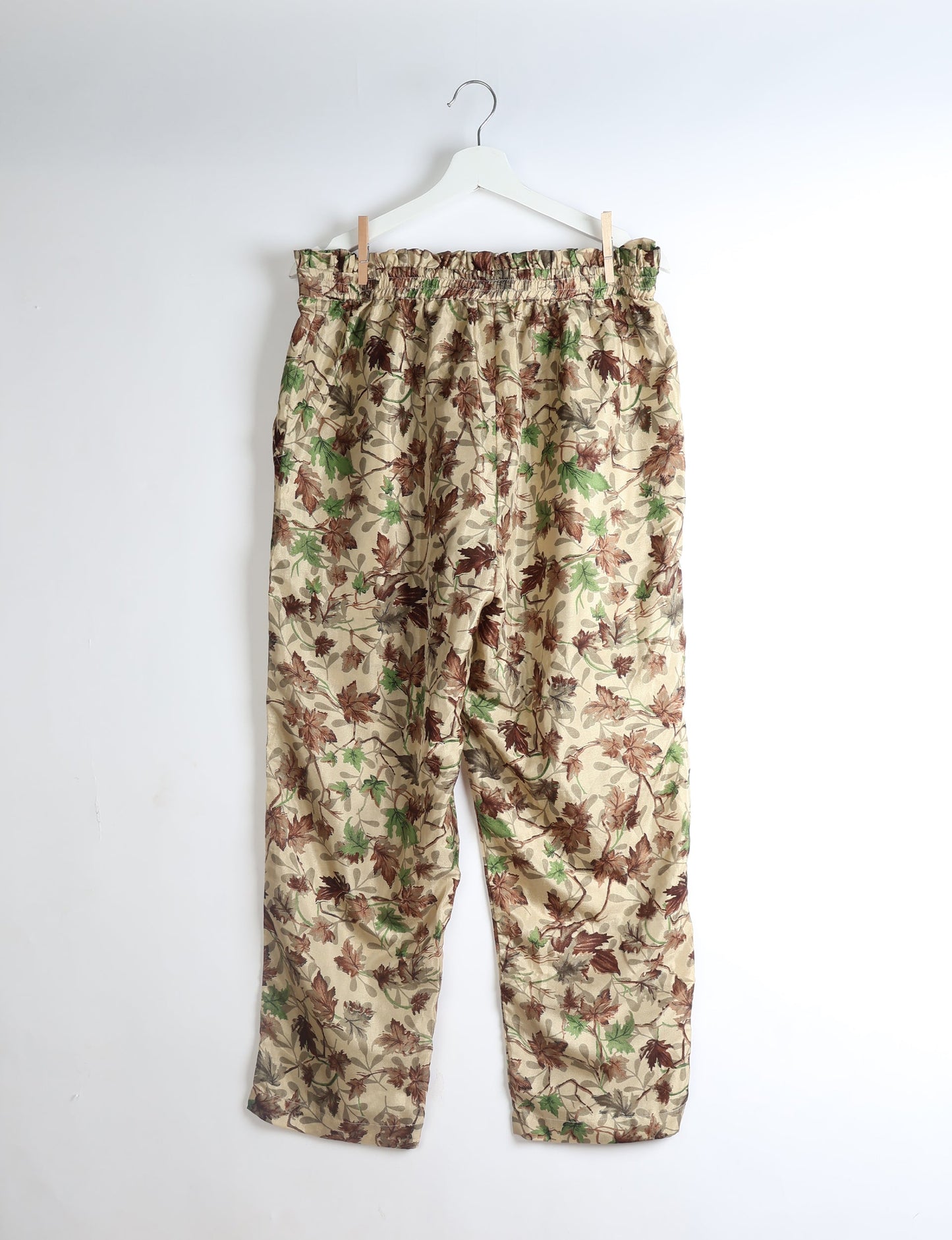 Beige paperbag high-waisted pull-on pants with brown and green leaf print, hanging on white hanger against white background
