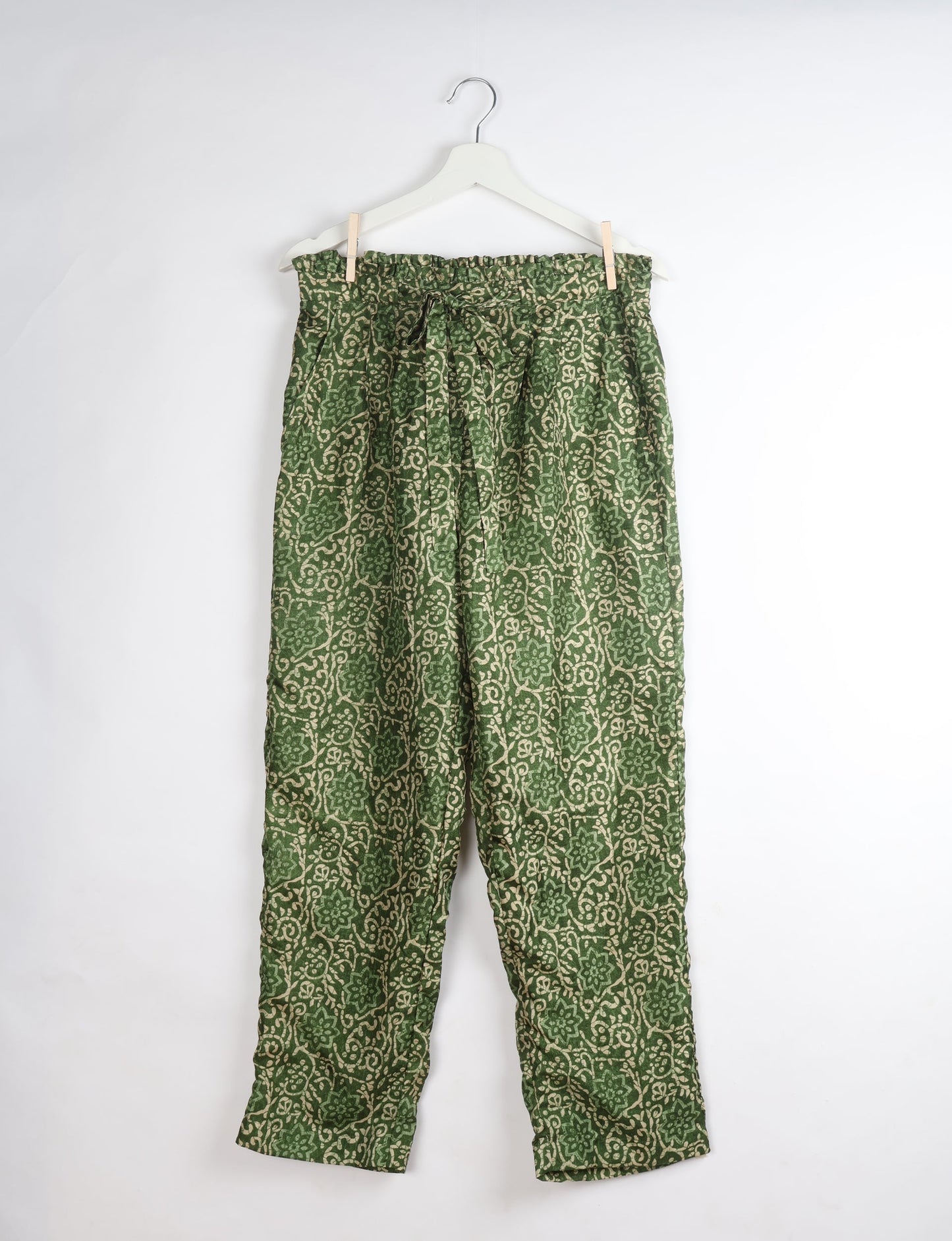 Green tropical patterned paperbag high-waisted pull-on pants with tie belt, hanging on white hanger, front view