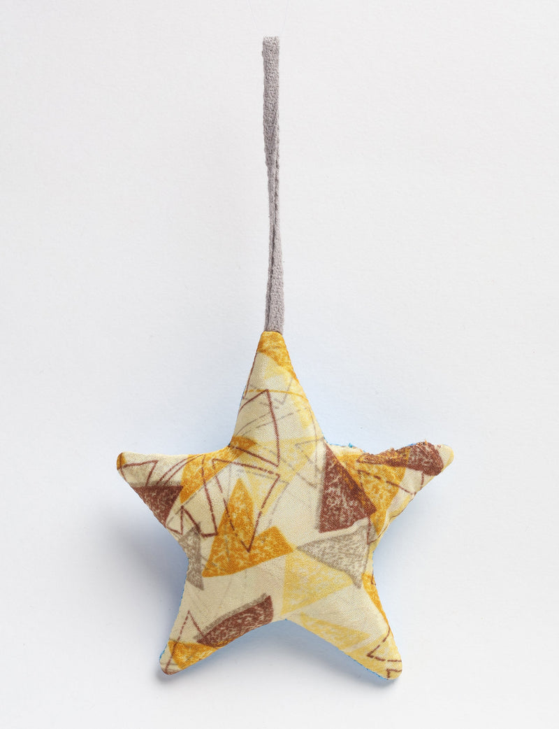 Beige fabric star-shaped bauble with abstract yellow and brown geometric patterns hanging by a gray loop