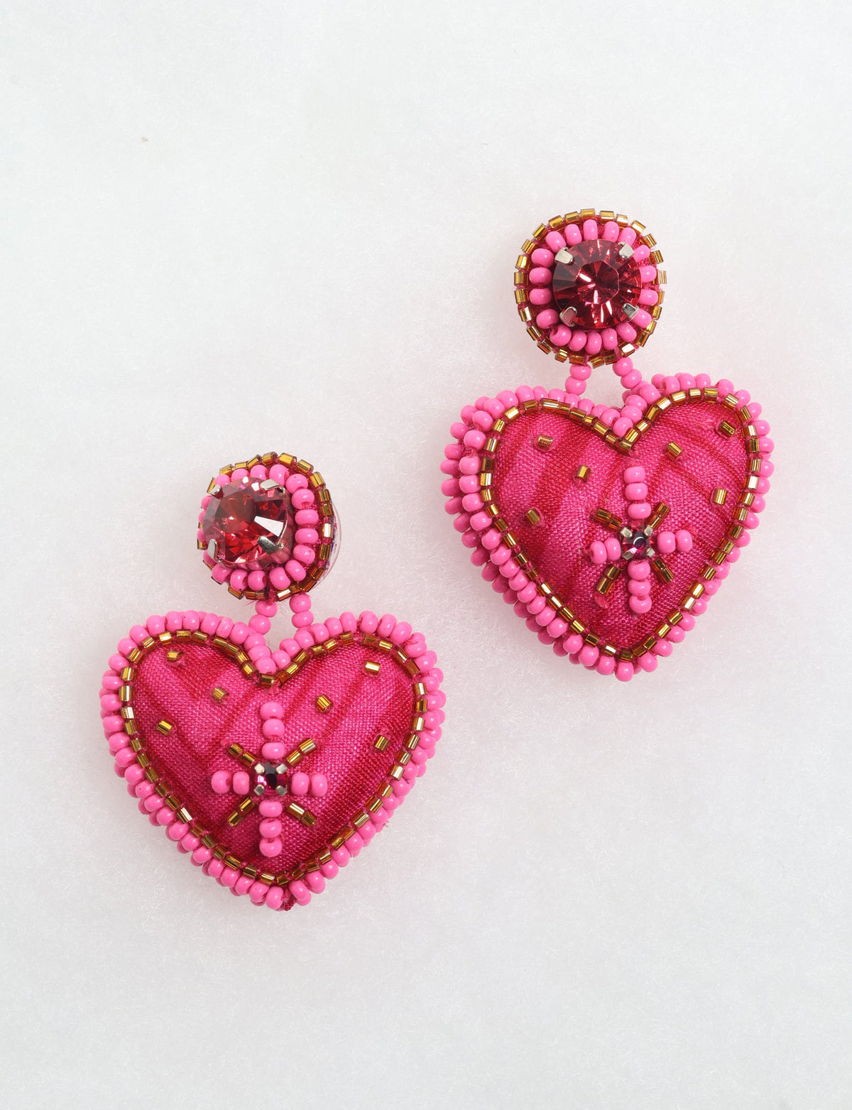Pink fabric heart drop earrings with pink and gold bead trim and red rhinestone studs, shown flat on white background