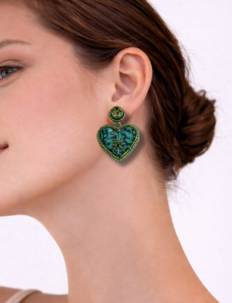 Green tropical heart-shaped drop earring with bead and sequin embellishments worn by a woman, side view