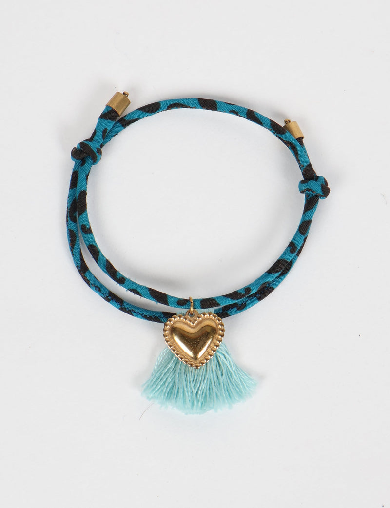 Blue and black abstract patterned rope bracelet with gold heart charm and light blue tassel, flat lay view