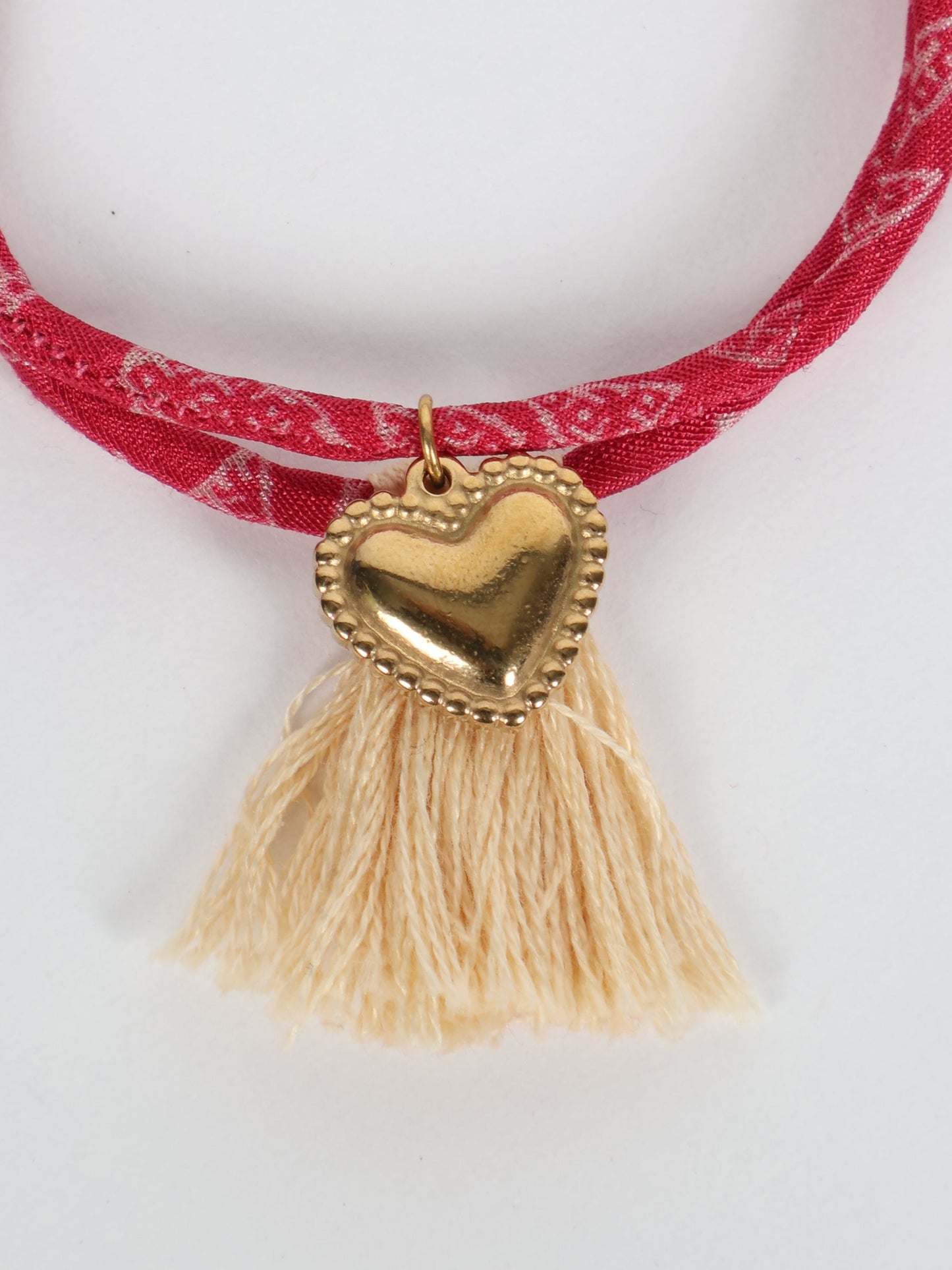 Handmade rope bracelet from recycled sari fabric with gold heart charm and tassels—eco friendly cloth, climate neutral fashion, and upcycled women’s clothing.