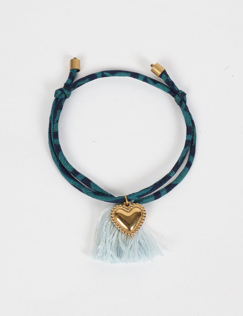 Blue and dark teal patterned rope bracelet with gold heart charm and light blue tassels, shown flat on white background