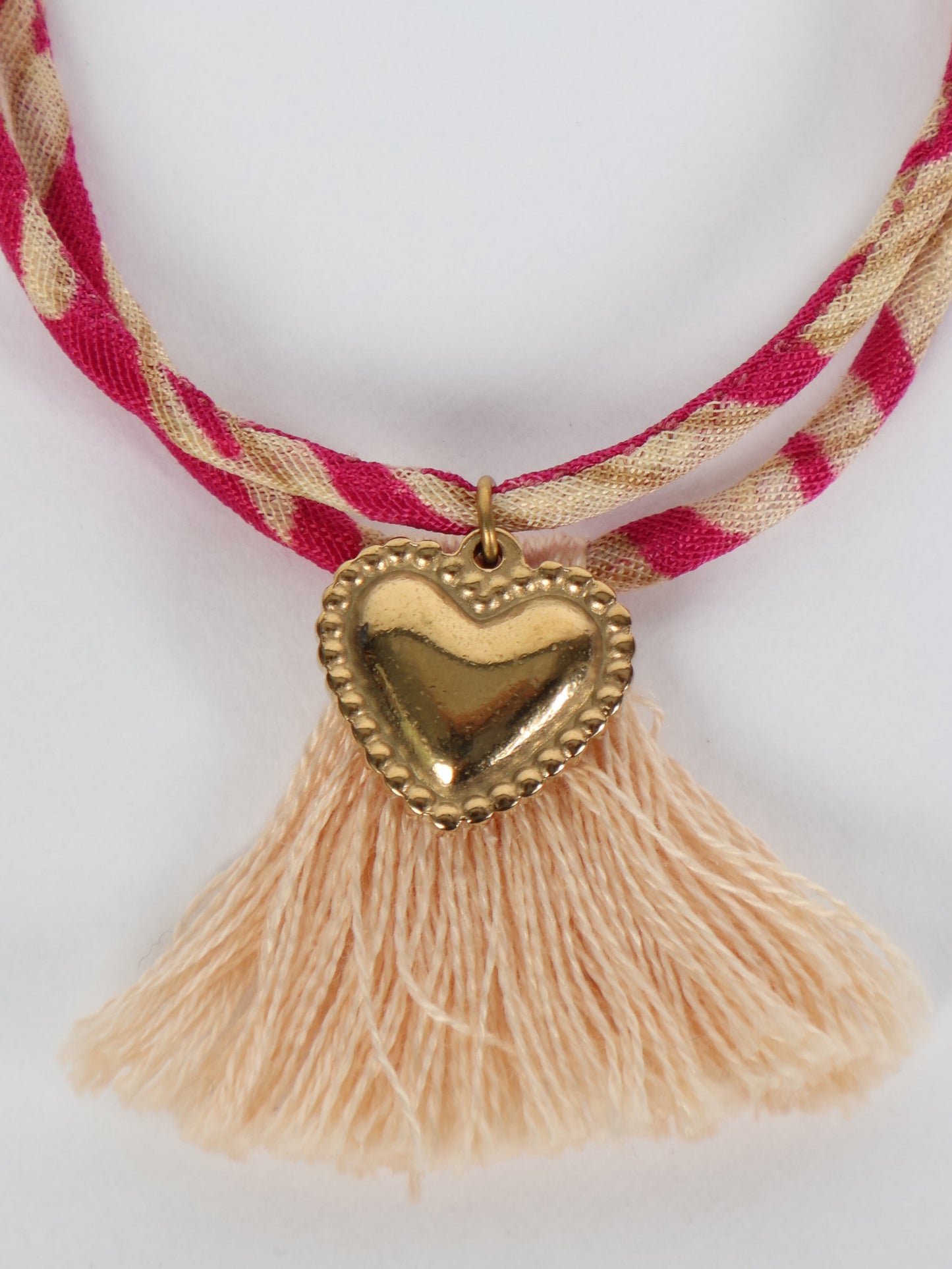 Handmade rope bracelet from recycled sari fabric with gold heart charm and tassels—eco friendly cloth, climate neutral fashion, and upcycled women’s clothing.