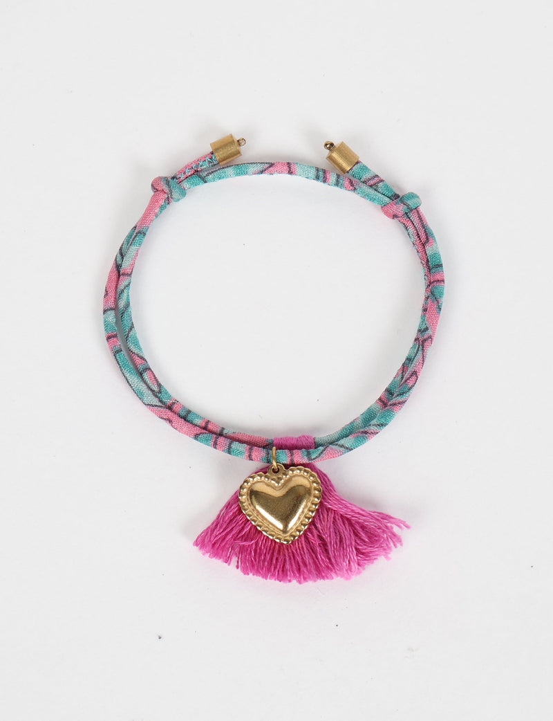 Pink and teal abstract patterned rope bracelet with gold heart charm and pink tassel, flat lay on white background