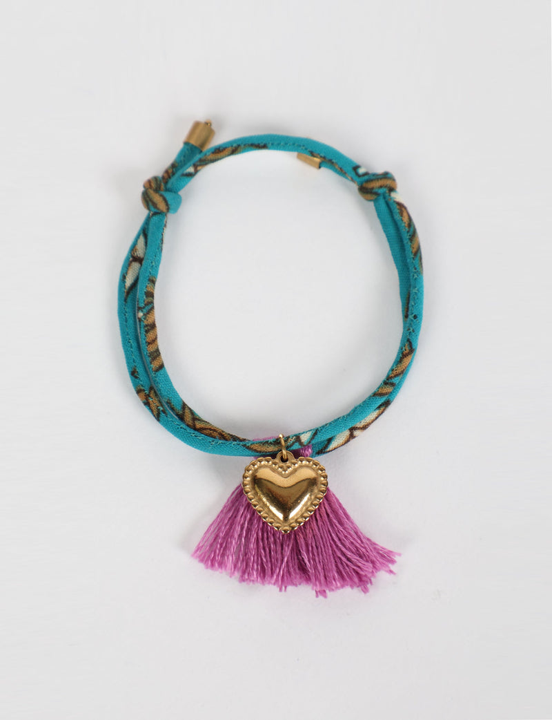 Blue patterned rope bracelet with gold heart charm and pink tassels, shown flat on white background