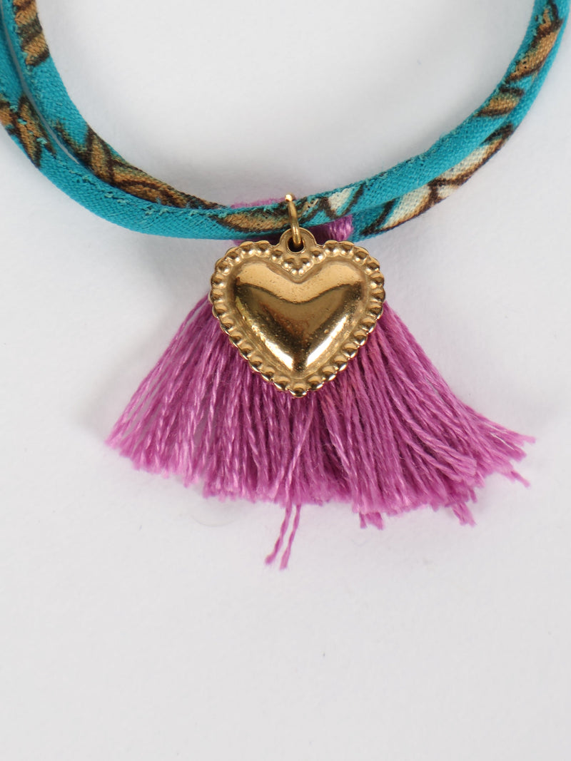 Blue and brown patterned rope bracelet with gold heart charm and purple tassels, close-up front view on white background