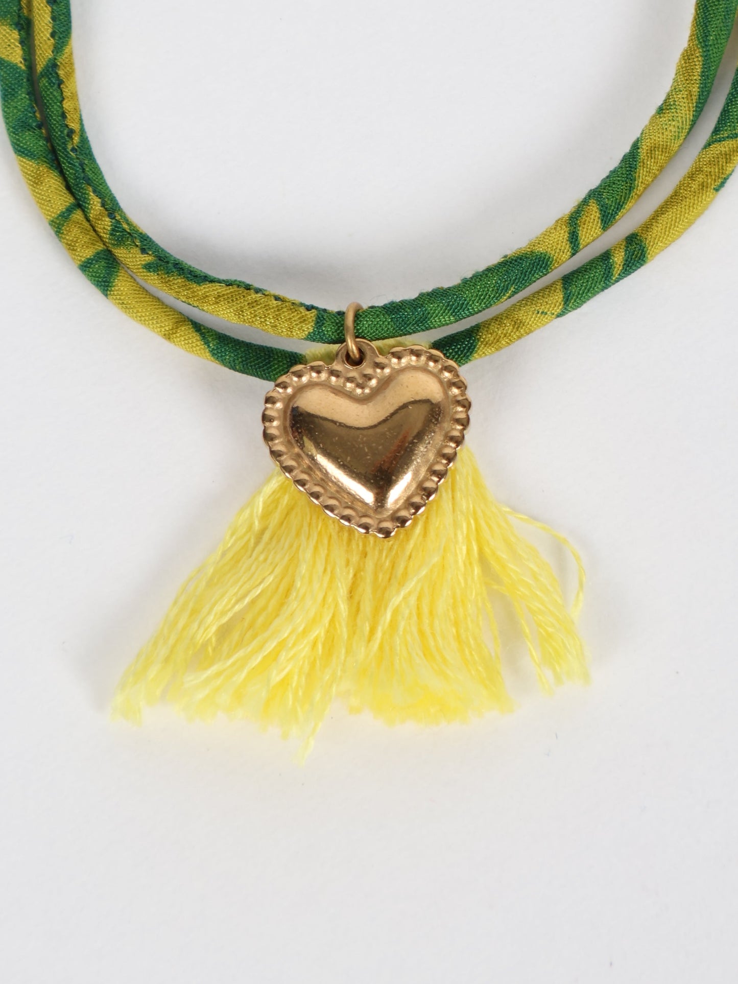 Handmade rope bracelet from recycled sari fabric with gold heart charm and tassels—eco friendly cloth, climate neutral fashion, and upcycled women’s clothing.