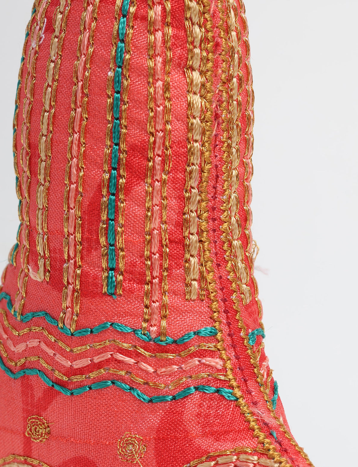 Red fabric bell ornament with gold, pink, and teal embroidered vertical stripes and wavy stitch patterns, close-up side view