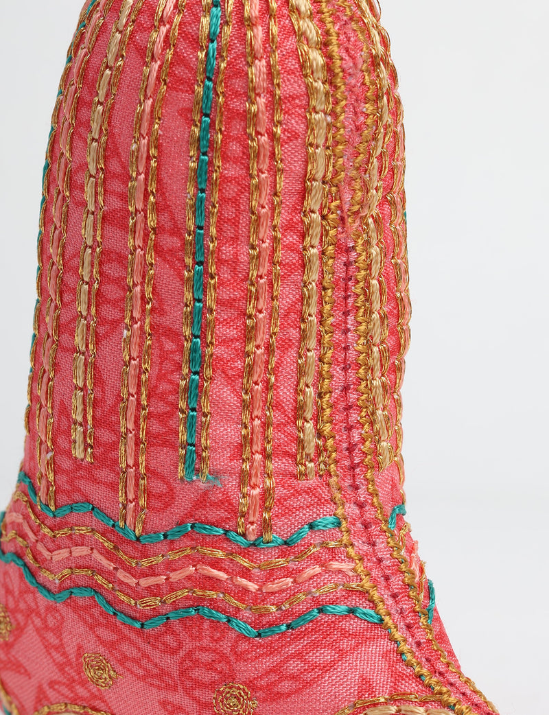 Close-up of a red fabric bell ornament with gold, peach, and teal embroidered vertical and wavy stitch patterns