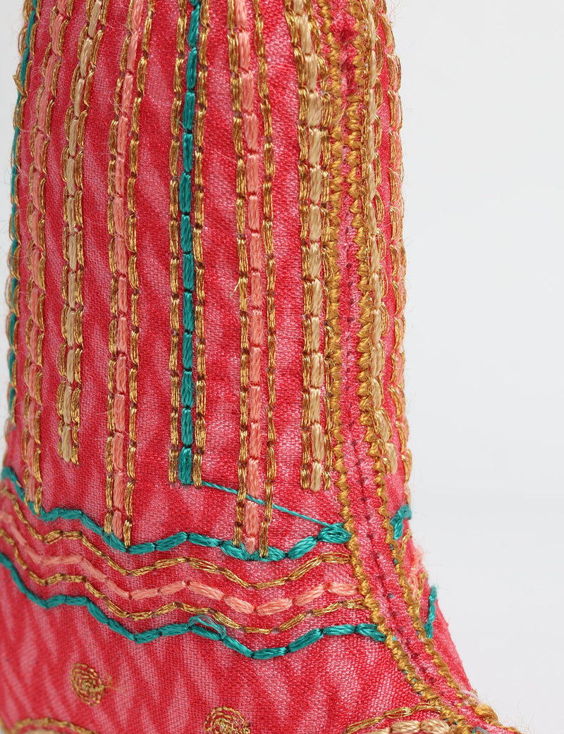 Close-up of a red fabric bell ornament with gold, peach, and teal embroidered vertical and wavy stitch patterns