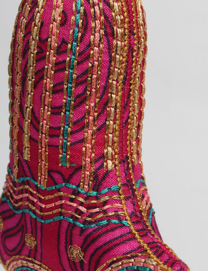 Close-up of a pink fabric bell ornament with gold, teal, and peach embroidered vertical stripes and floral patterns