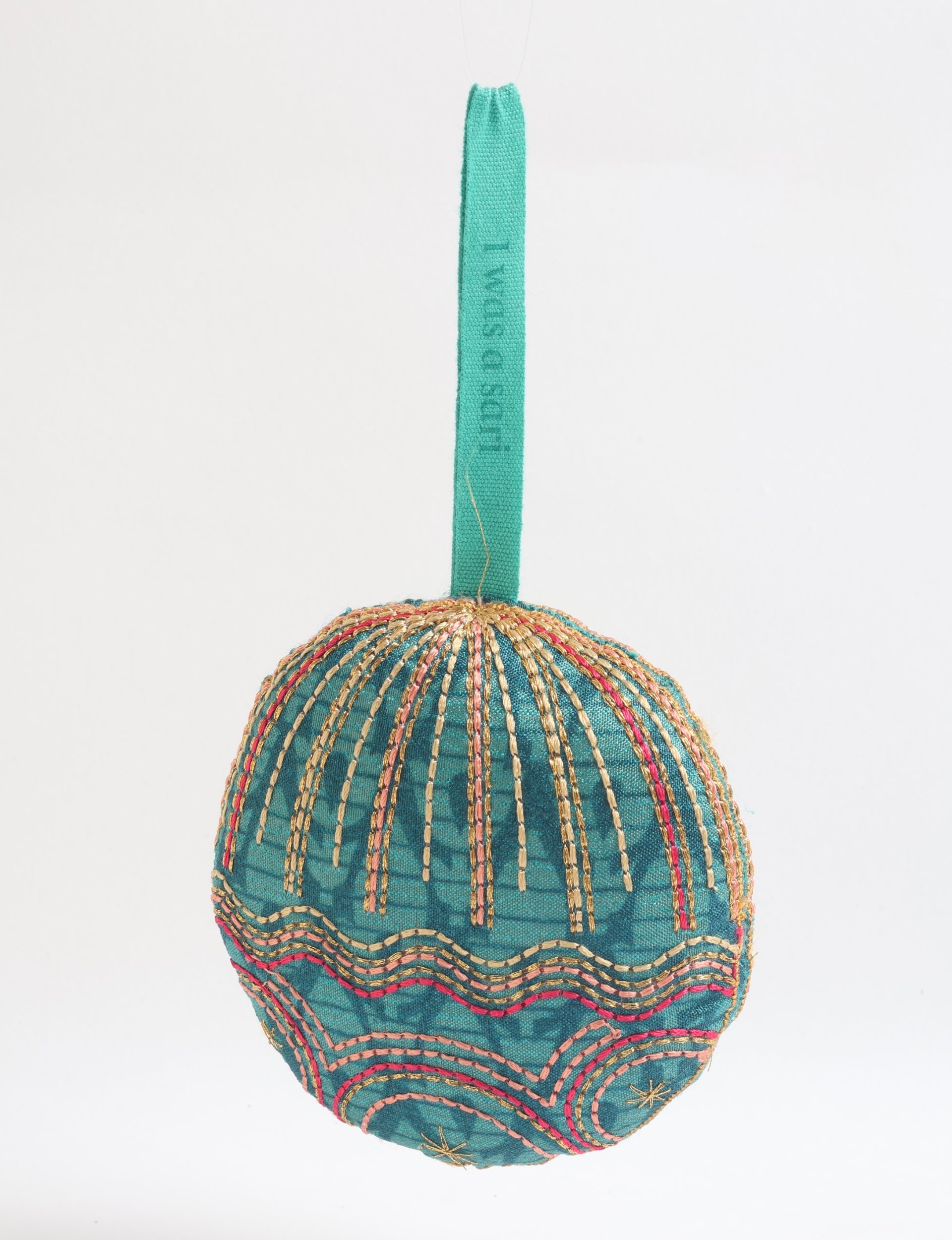 Round fabric ornament in green with gold and pink stitched patterns, hanging by a green fabric loop with text