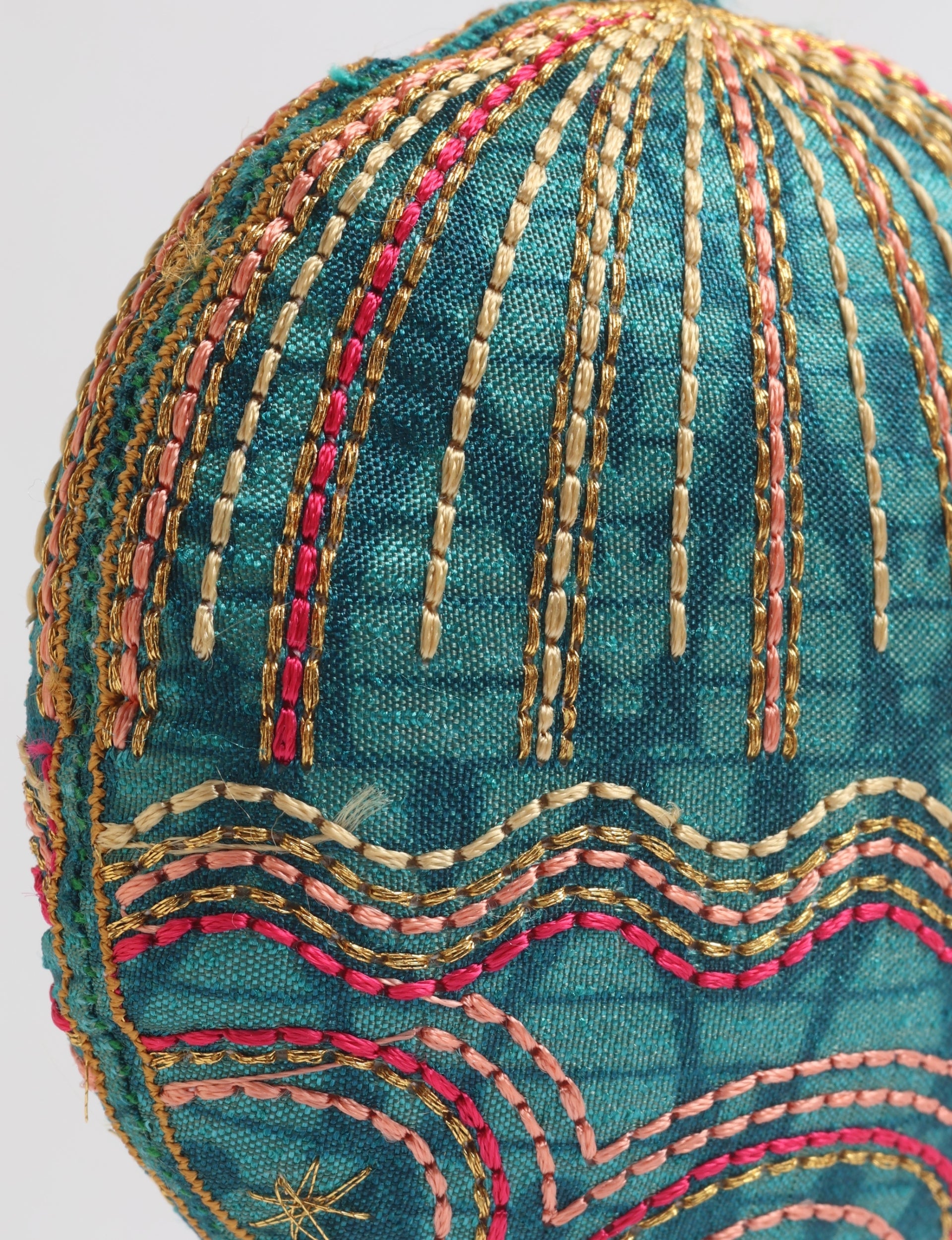 Close-up of a teal fabric full moon ornament with gold, pink, and cream embroidered stripes and wave patterns