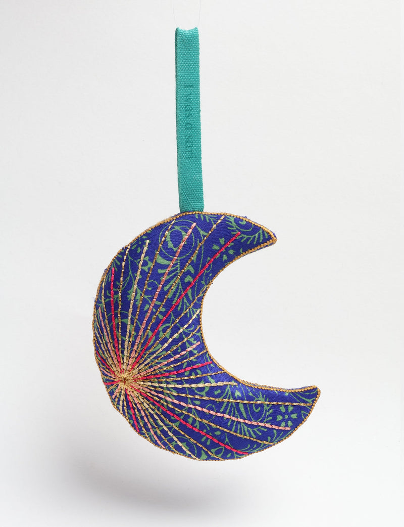Blue fabric crescent moon ornament with green tropical pattern and multicolored stitched details, hanging by teal loop