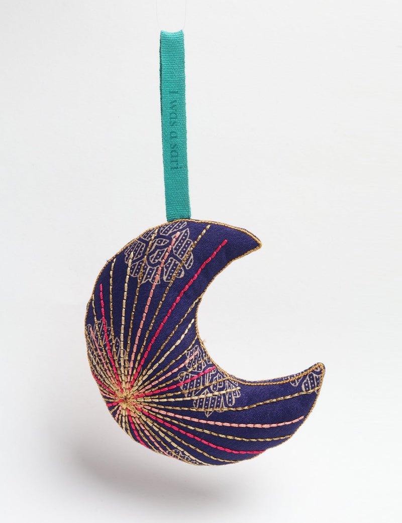 Blue fabric crescent moon ornament with gold, pink, and red floral embroidery and a teal hanging loop against white background