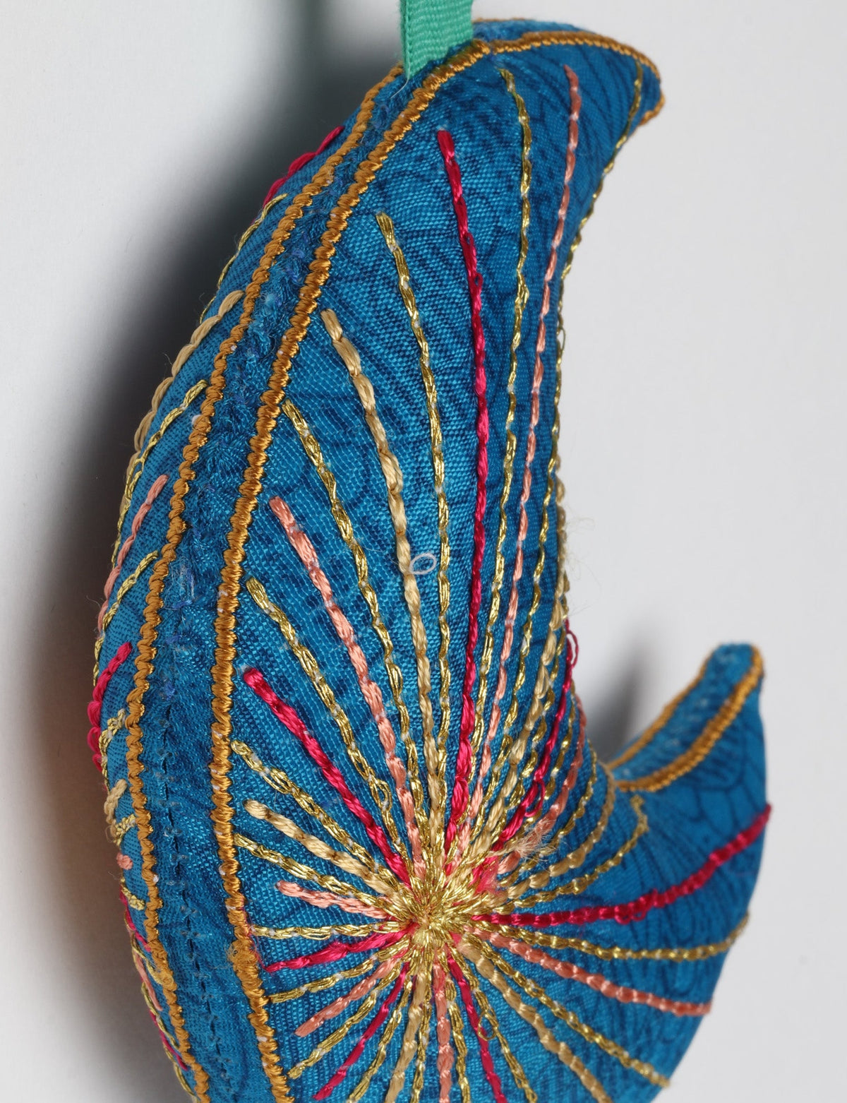 Blue fabric crescent moon ornament with multicolored stitched lines and a matching blue hanging loop against white background