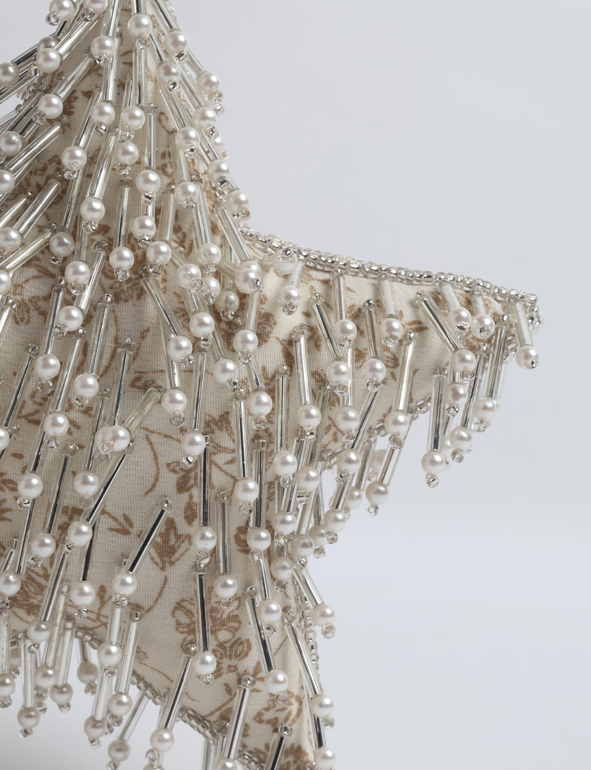 Beige fabric star ornament with brown tropical print, decorated with silver tubes and pearl beads, close-up view