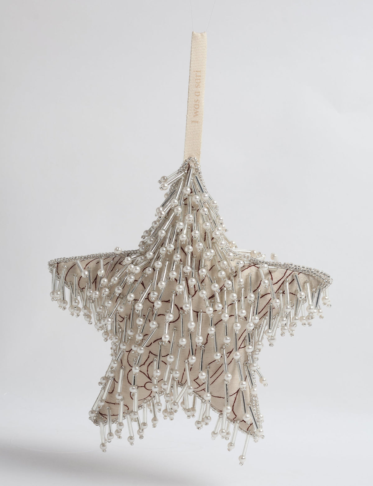 Beige fabric star ornament with brown floral print, decorated with silver beads and pearl-like accents, hanging by a beige