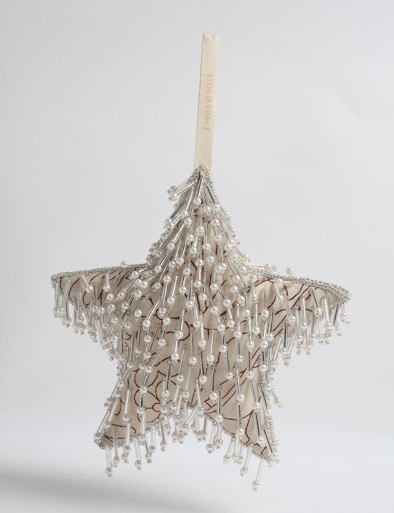 Beige fabric star ornament with brown floral print, decorated with silver beads and pearl-like accents, hanging by a beige