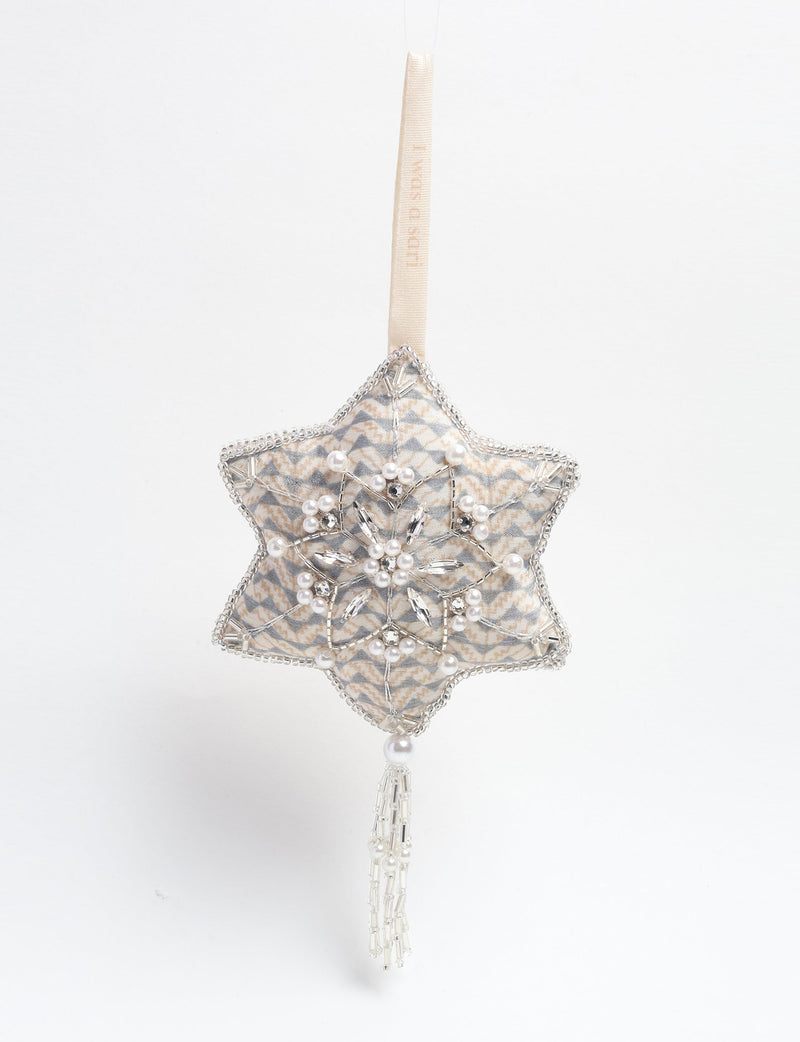 Silver fabric snowflake ornament with pearl and bead embellishments, hanging by a cream ribbon loop with tassel detail