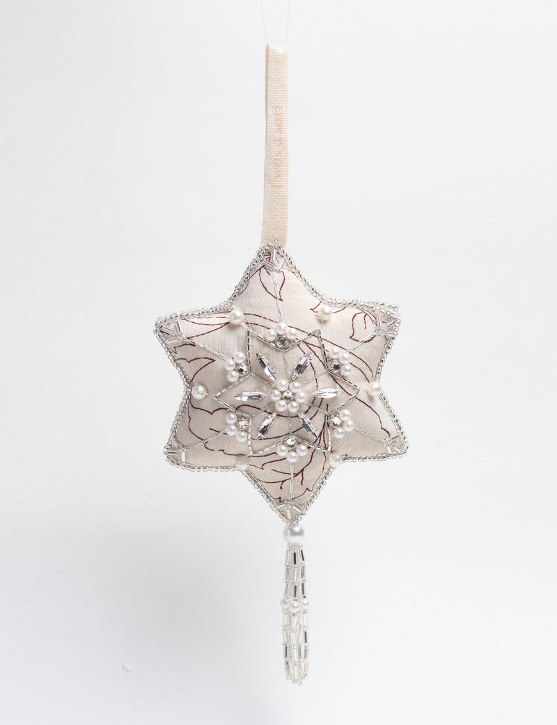 Silver fabric star ornament with beaded snowflake design, pearl accents, and hanging tassel, shown front view on beige loop