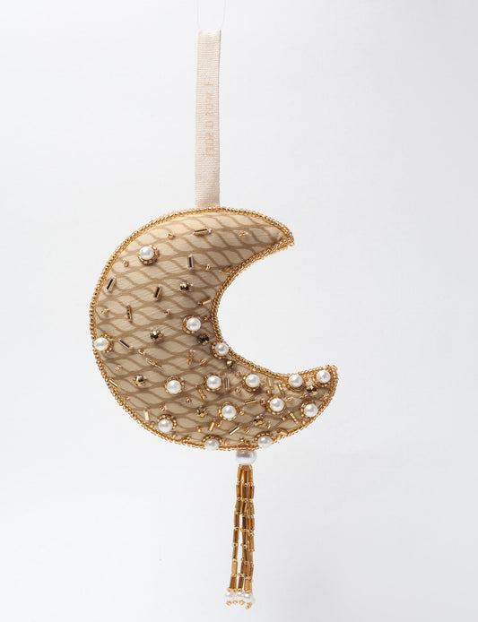A crescent moon ornament made from ivory and cream recycled fabric, filled with organic cotton, embellished with gold stones and beads. This recycled clothing piece aligns with circular fashion, earth friendly clothing, and fashion revolution ideals, crafted to support repurposed clothing and eco friendly fashion.